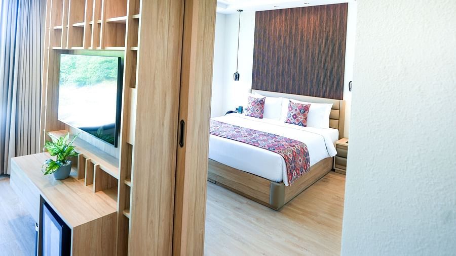 A portrait image of a suite featuring a living area with a wall-mounted television, a minibar, and a large bed situated in the background - NAMAMI BY ZENQ BANKHANDI