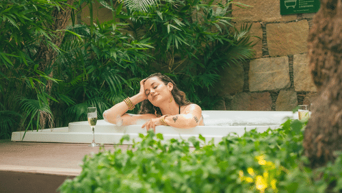 Woman relaxing in a private outdoor jacuzzi surrounded by lush greenery and stone walls, creating a tranquil and secluded spa-like environment - Ananta Spa and Resort, Pushkar.