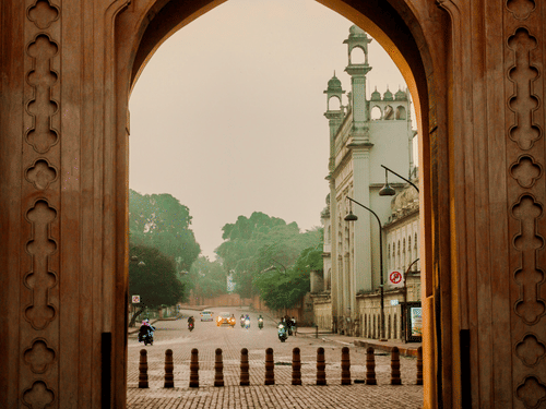 A framed view through a grand scalloped arch looking out onto a misty street with trees and minarets in the distance.
