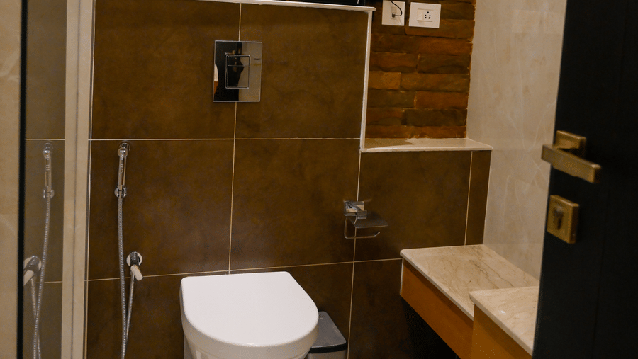 An indoor shot of a bathroom focusing on a white toilet fixture against dark wall tiling and an upper textured section at Tiara by MPS.