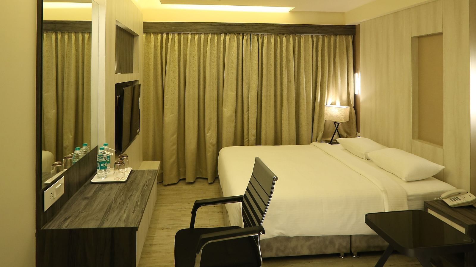 Premium Room shown with a king size bed, desk, chair, and mirror, illuminated by warm lighting - TGI SPS Grand, Coimbatore
