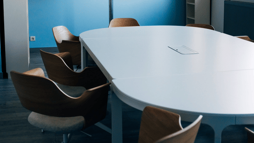 Modern meeting room with blue walls, round table, and display screen.