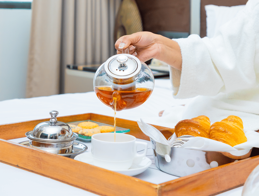 A wooden breakfast tray with plates cups and cutlery placed near a window at The Suryaa, New Delhi.