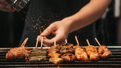 A man sprinking salt over pieces of meat in skewers