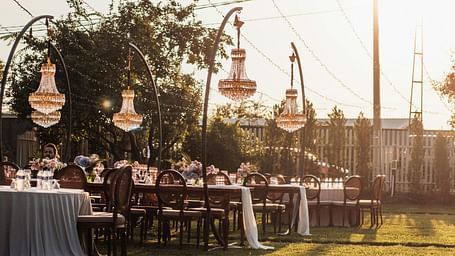 A beautiful lawn area with tall poles holding the decorative strings with a bright sun setting in the background.