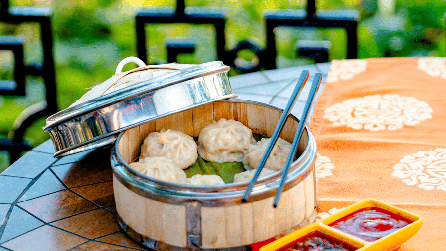 A bamboo steamer filled with fresh dim sum served on an outdoor table at Ming Dynasty, part of the Noor-Us-Sabah Palace, Bhopal, accompanied by dipping sauces.