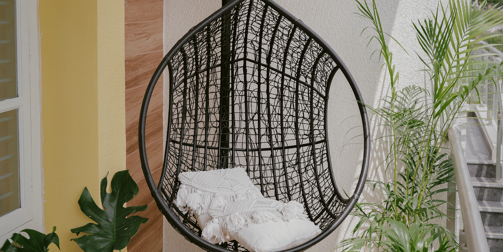A hanging chair with a white cushion on a balcony with potted plants  | Adhyaya Heritage Reverbed