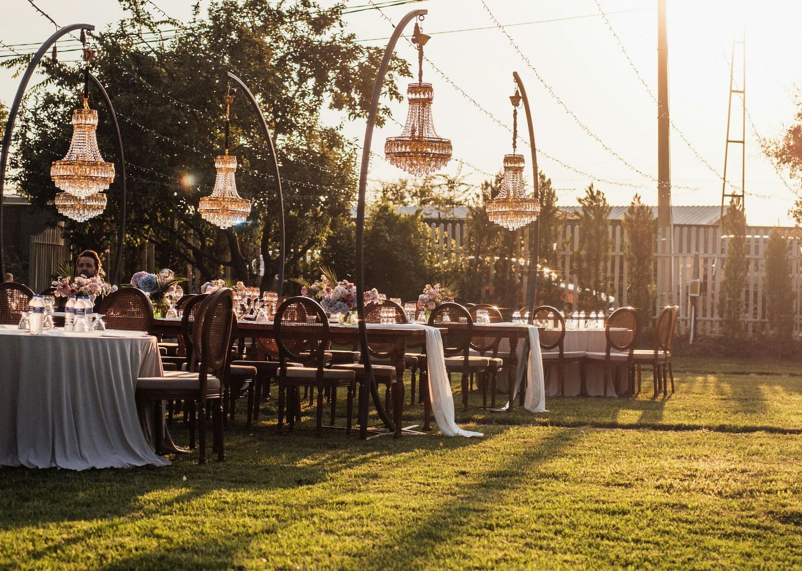 Outdoor dining area at sunset with string lights and banquet tables.