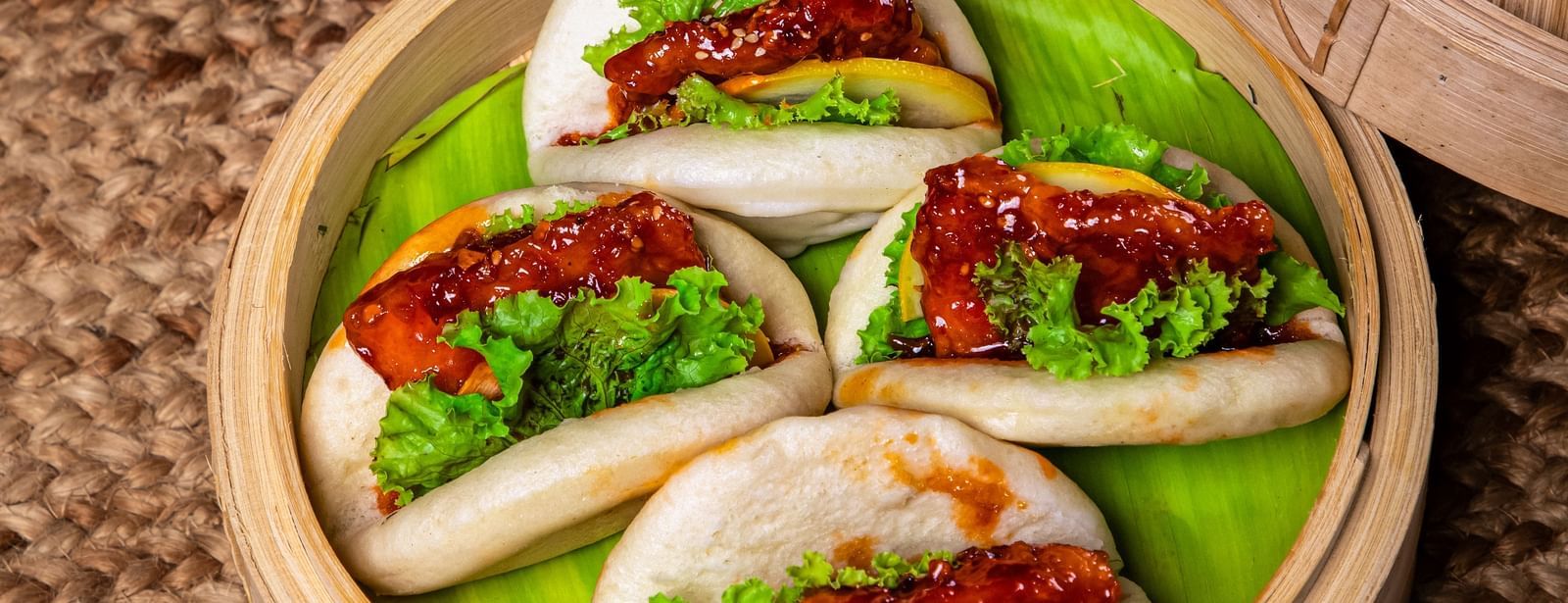 A bamboo steamer filled with buns stuffed with vibrant vegetables and proteins, accompanied by a tray of shredded purple cabbage and garnishes on a woven mat surface at The Hamuse Hotel, Kodaikanal.