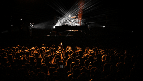 Dark concert stage with dramatic spotlight shining over a large crowd.