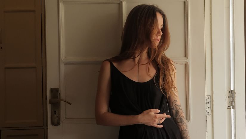  A woman in a black dress standing by an open door, looking away from the camera.