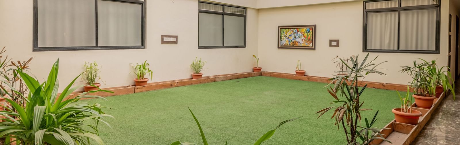 Corridors of Hotel Highway King, Behror, separated by an area covered by grass in the center and lined by potted plants.