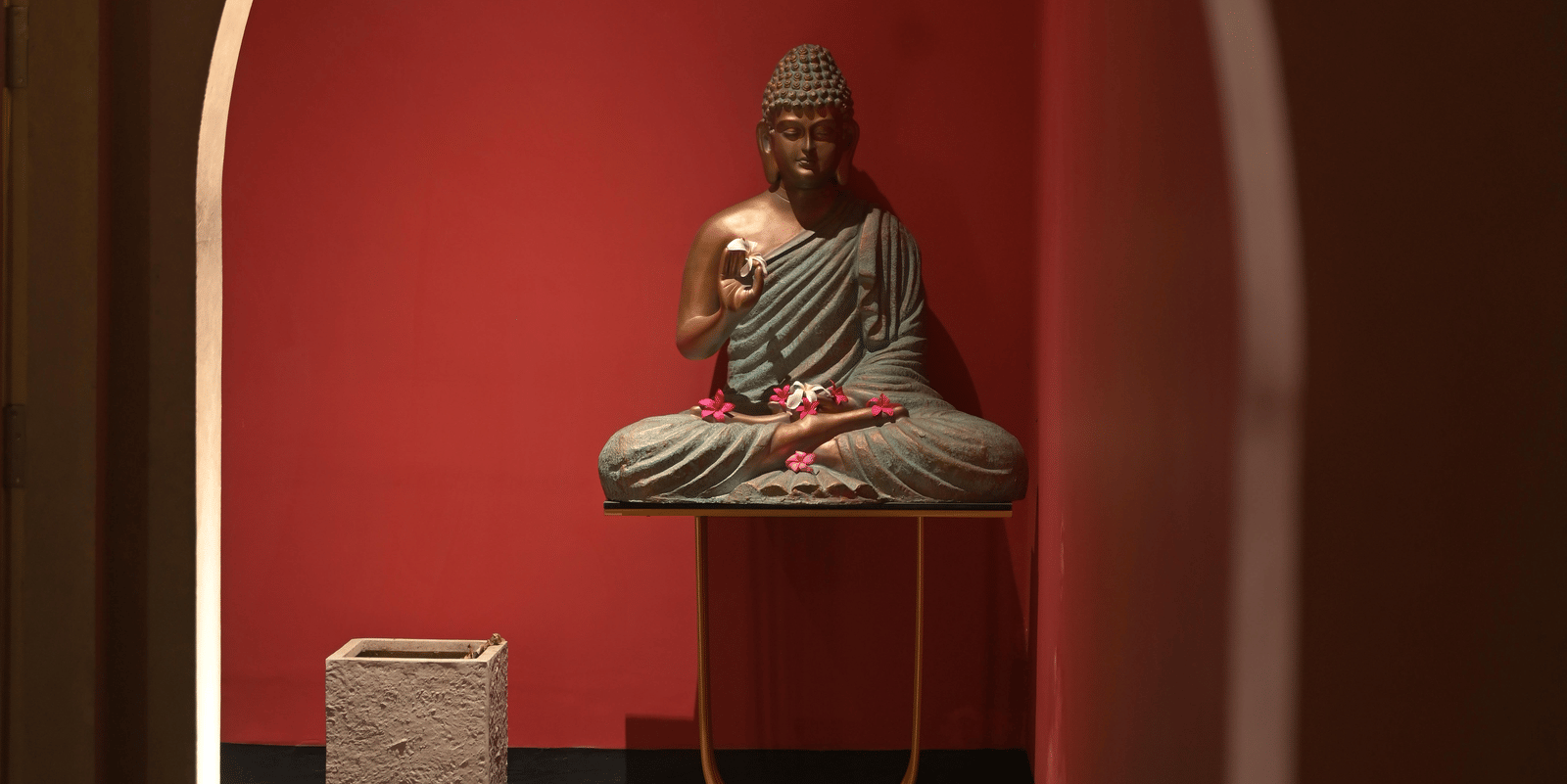 A corridor featuring a niche with a Buddha statue and red accent wall at Hotel Sonar Bangla Mayapur.