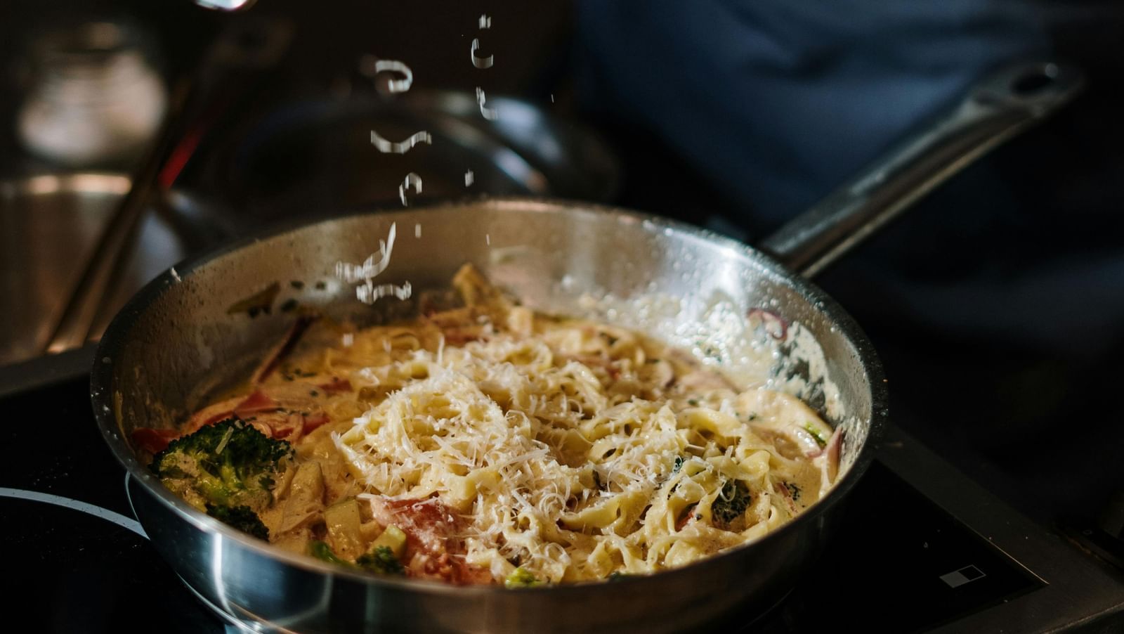 Close up of a person grating cheese into a pan of food.