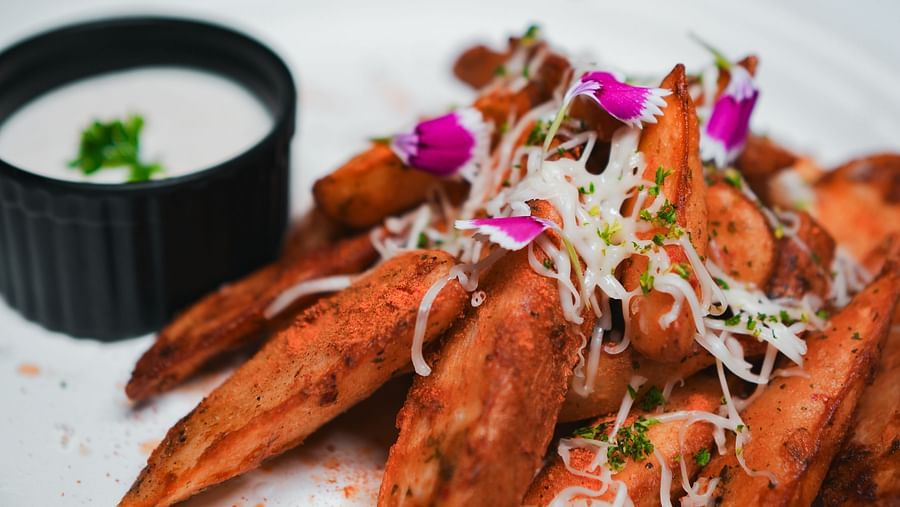 Crispy seasoned wedges topped with shredded cheese and microgreens, served with a creamy dip at D Café, Dip Holidays.