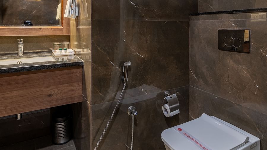 Modern bathroom with wall-mounted toilet and dark-toned tiles at Hotel Highway King, Bilaspur.