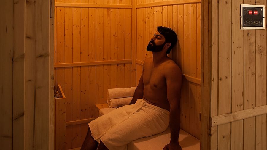 Person sitting in a wooden sauna, warm light, relaxation setting - Shreyas Retreat