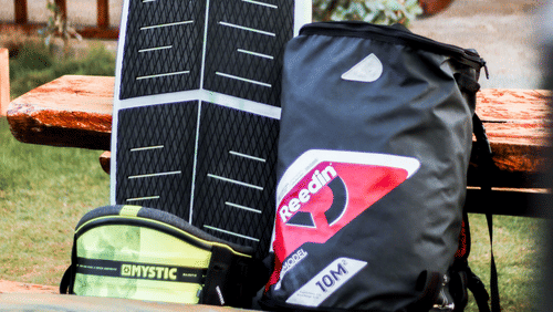 Surfboard, kiteboard, and water sports gear arranged outdoors near a beachside property.