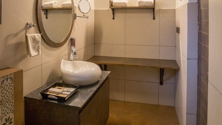 Bathroom with circular mirror and wooden vanity setup at Nirantara Resort & Spa