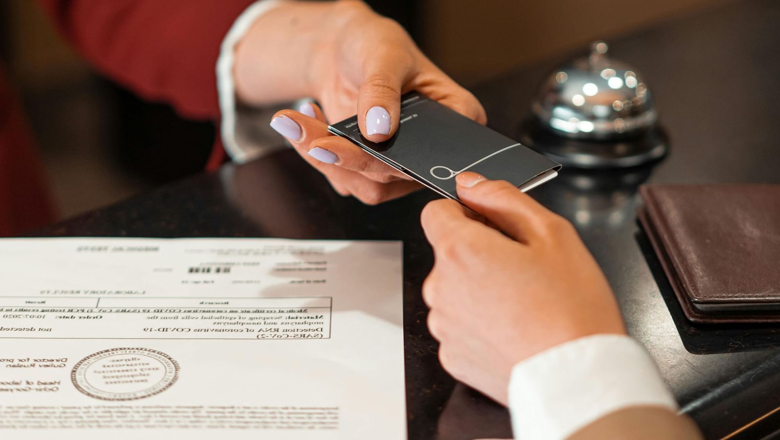 A receptionist handing over a card to a customer, a paper, bell and wallet on the table beneath