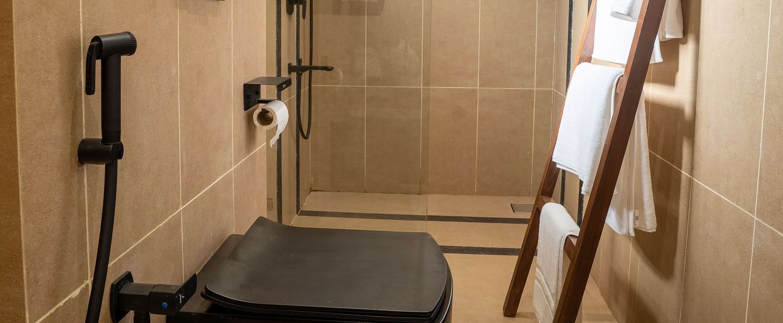 Compact bathroom featuring black sanitary ware, glass shower area, and wooden ladder towel rack at Kssemya.