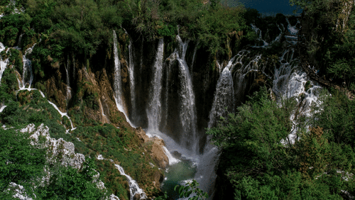 A series of waterfalls falling from tall verdant mountains