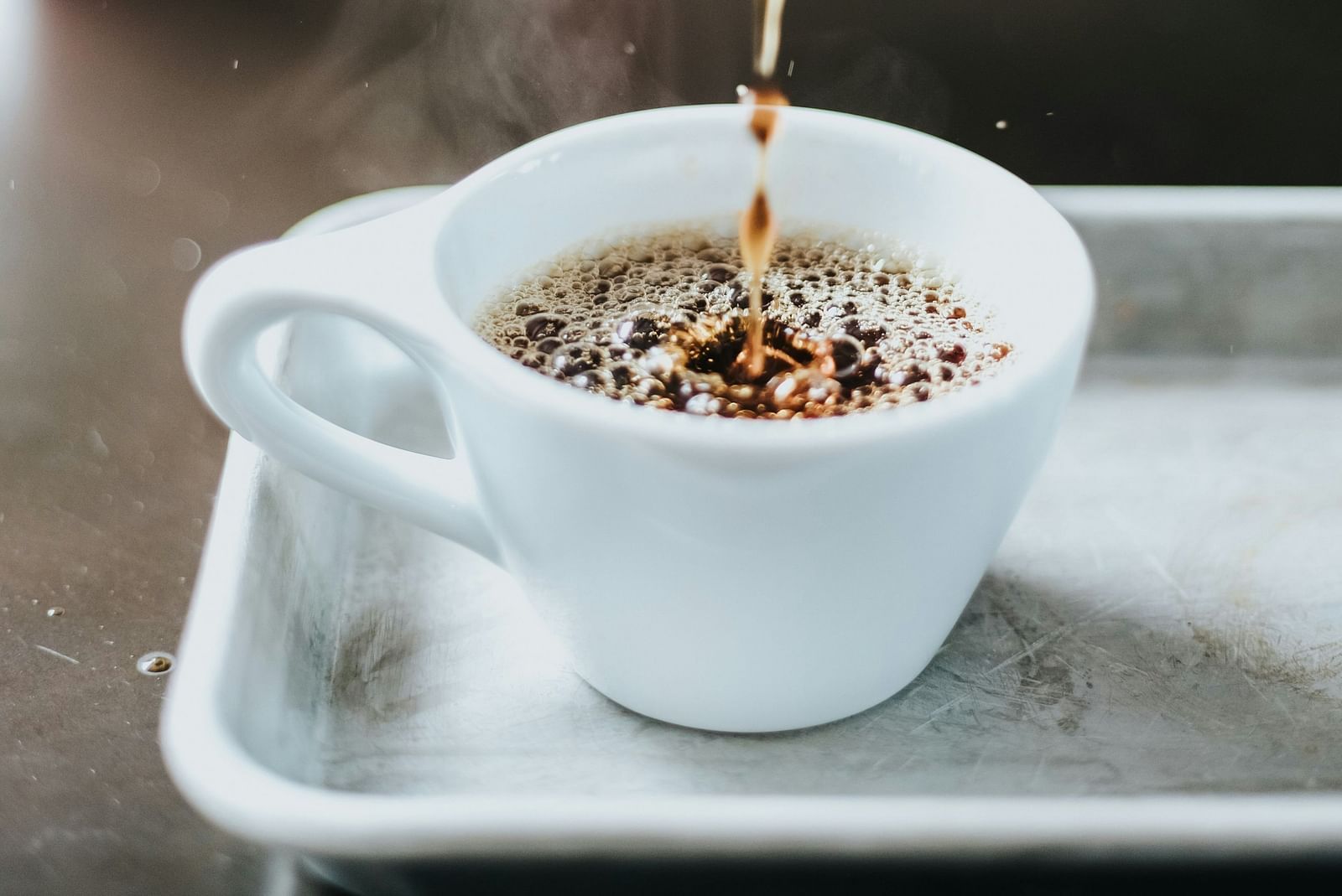 A drip of coffee being poured in a white cup in a tray