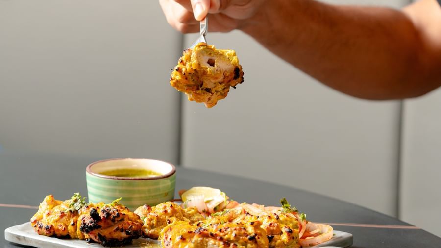 Hand holding a fork with food, showing a close-up of a dish | Pravasa Hotel, Vijayapura