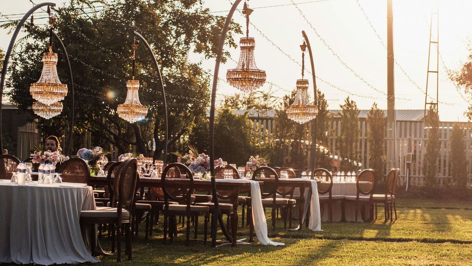 Outdoor dining area at sunset with string lights and banquet tables.