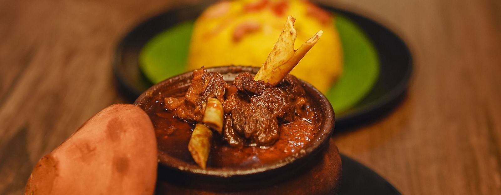 image featuring a mutton preparation served in an earthen pot with yellow rice - Dip Holidays, Birbhum