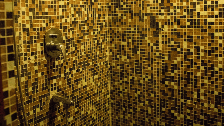 A bathroom with Mosaic tiled walls with a hand shower mounted on the wall at Benzz Park, Vellore.