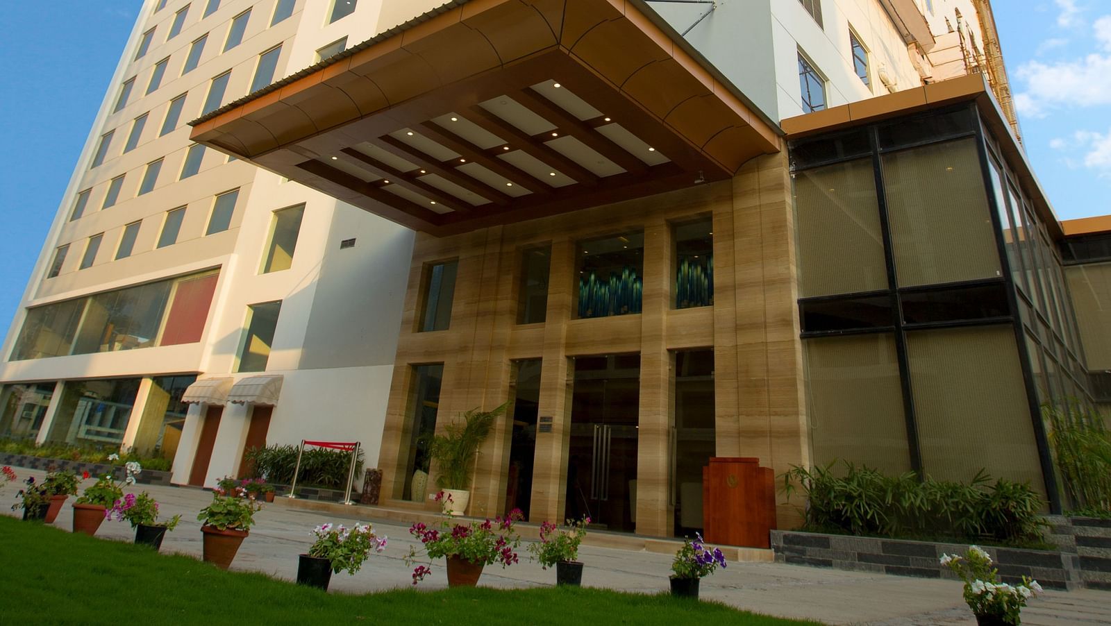 An exterior shot of our hotel taken from a lower angle with a lawn area in the foreground - Ramada by Wyndham, Ghaziabad, Vasundhara