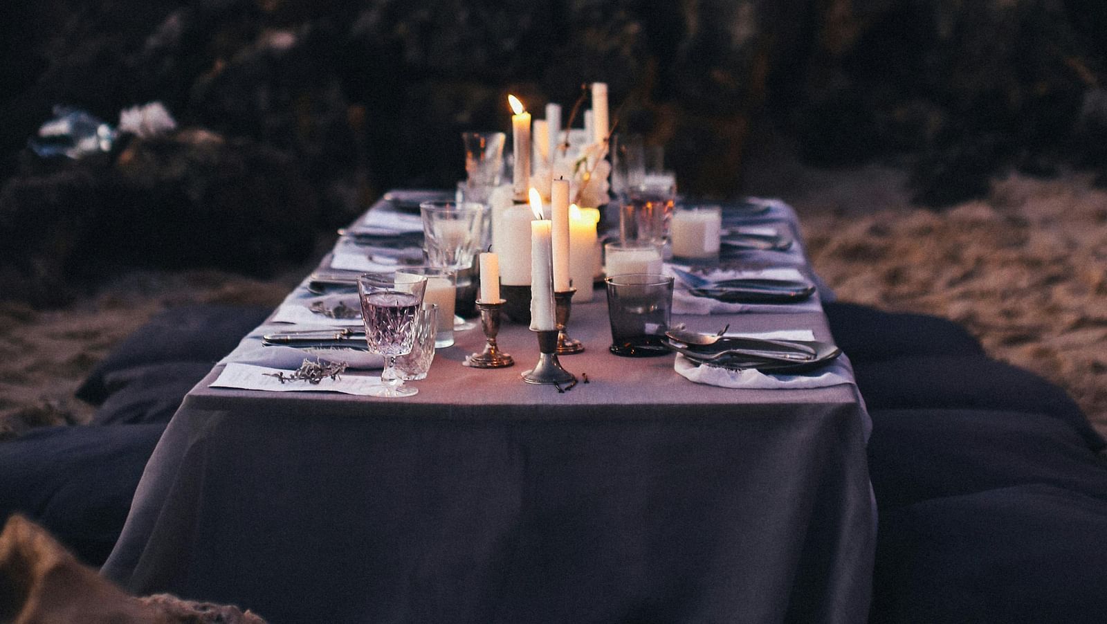 A dining arrangement by the beach with cutlery kept on a table and forest cover in the background.