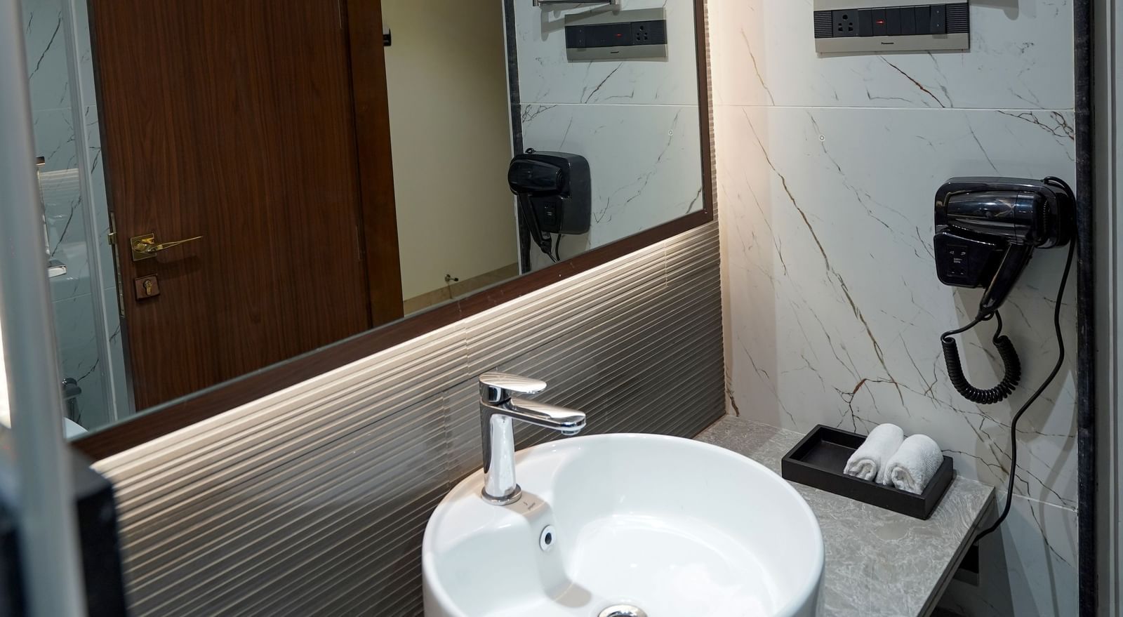 A modern bathroom featuring a neat vanity area along with a back-lit mirror at M2 Square by Monday Premium.