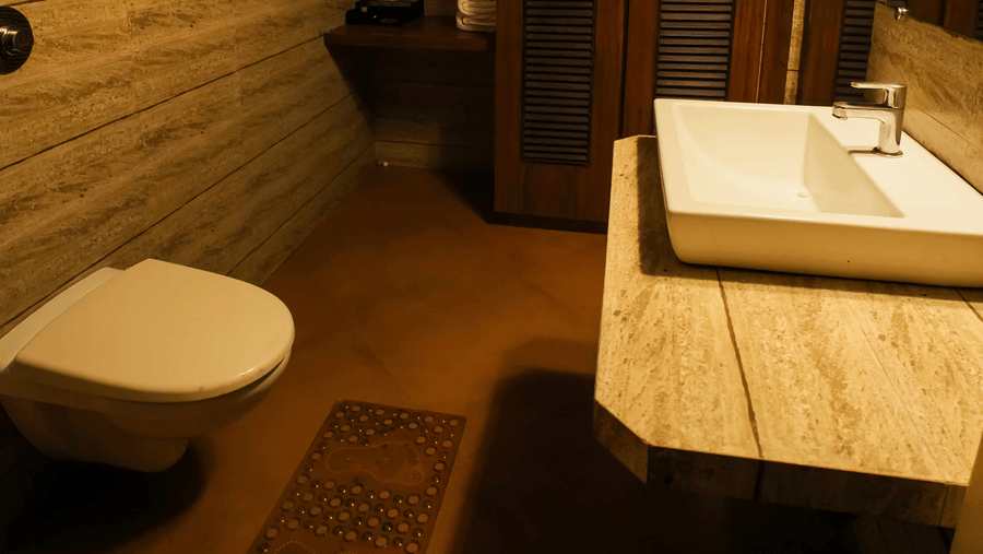 A compact washroom at Adamo The Village showcasing a countertop basin, toilet, and wooden-textured interiors.
