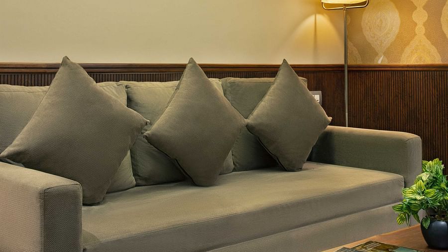 Image of Coral Suite at Coral Reef Hotel and Spa in Port Blair featuring a three seater sofa along with a coffee table in front of it and wall hangings over it and a lamp in the corner