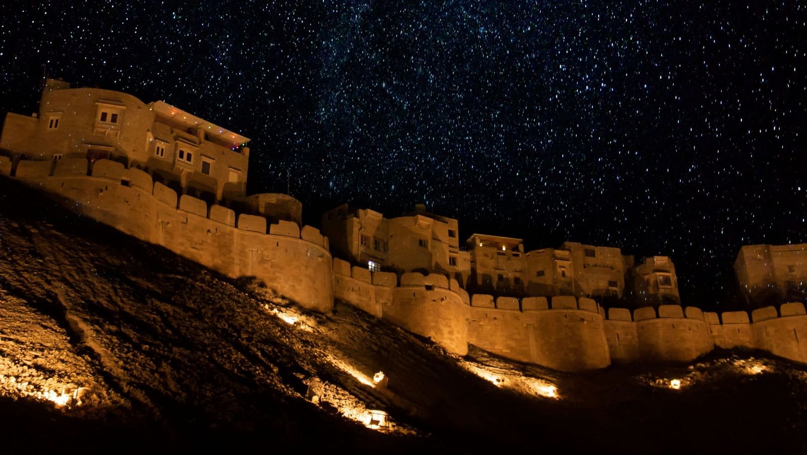 A far out view of a palace with lights on in the night and the stars bright in the sky in the background