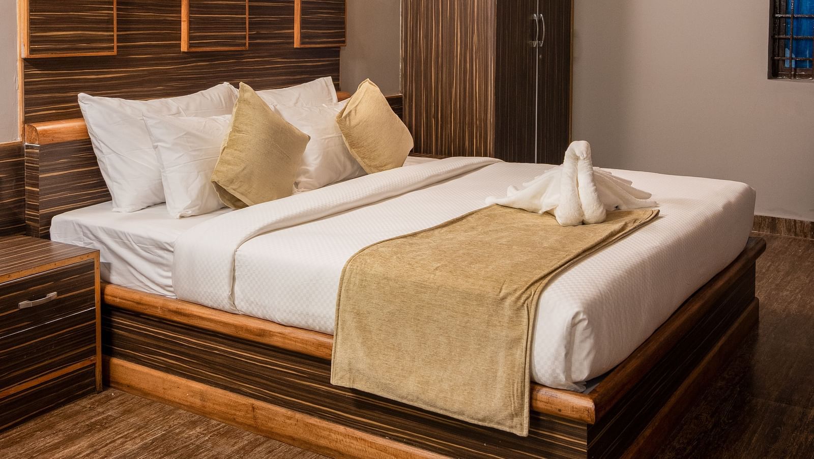 A comfortable bedroom is furnished with a large bed featuring a wooden headboard, soft lighting, and a view of the room's interior | Standard Room | RD's Nature Retreat, Bangalore
