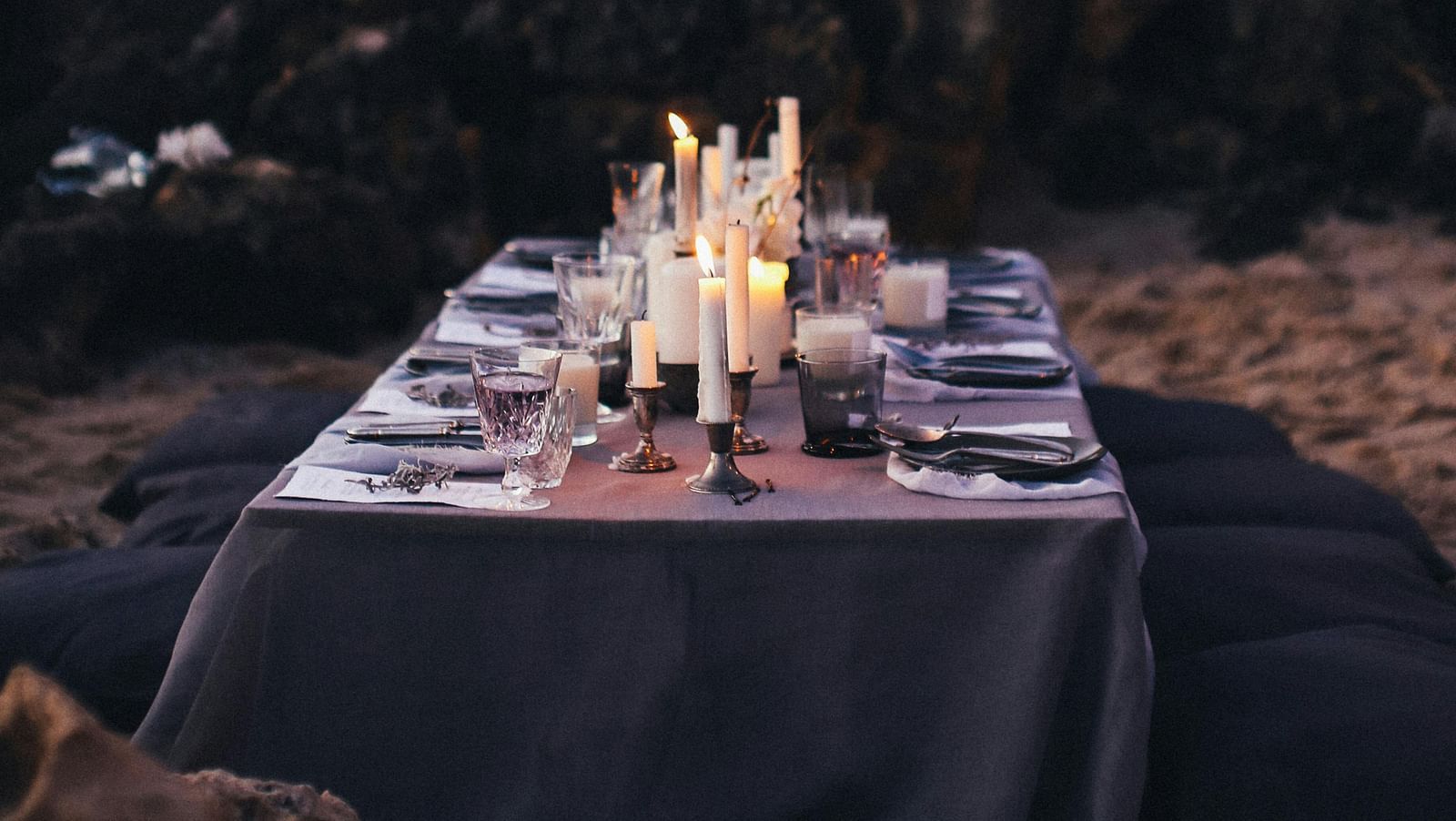 A dining arrangement by the beach with cutlery kept on a table and forest cover in the background.