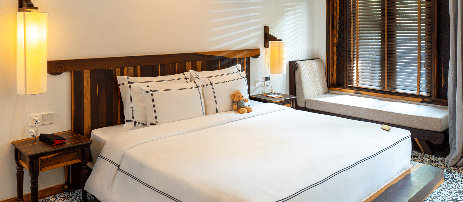 A bedroom at Alibu Resort Nha Trang featuring double size bed, bedside table  with lamps on either side, and a llounger bed near the window.