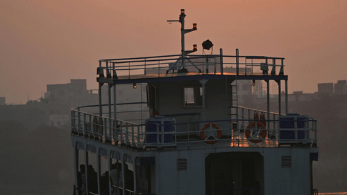 a small ferry boat sailing in a water body with orange hues of sunset in the background.