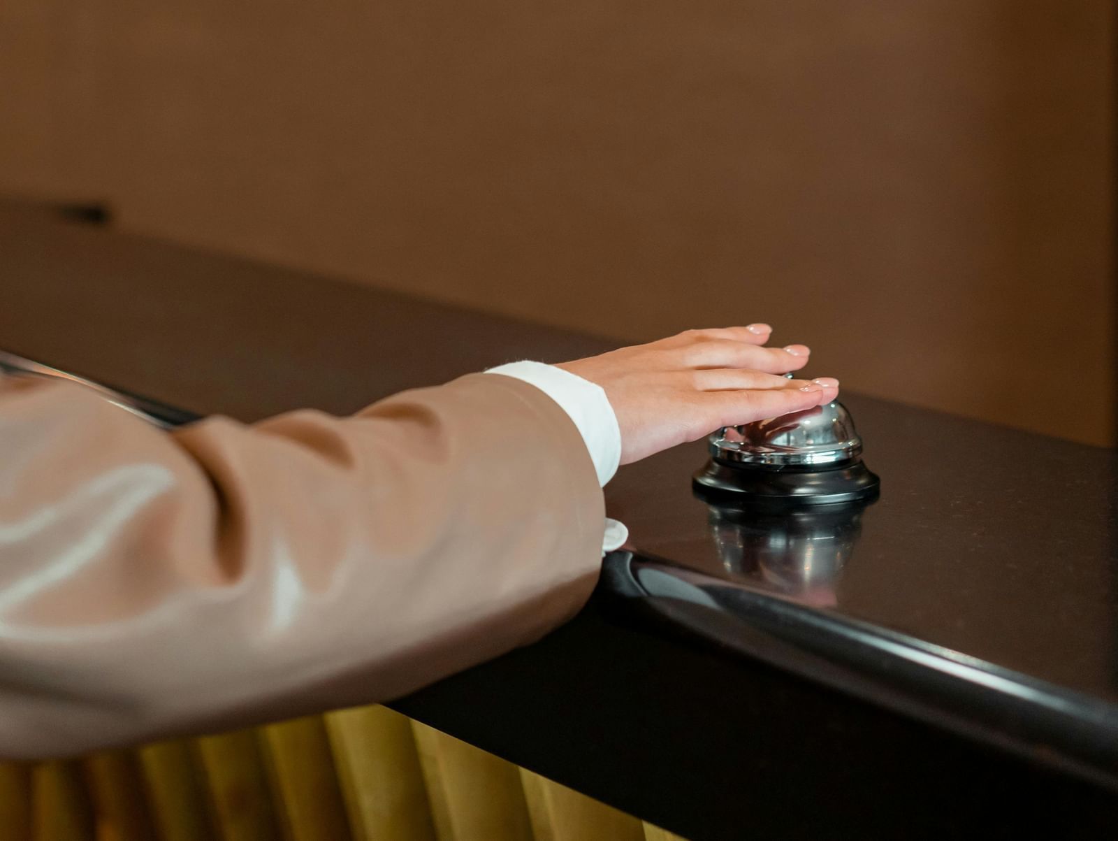 A hand reaching to press a control button on a modern wall panel, possibly for an elevator or room service, in a minimalist setting.