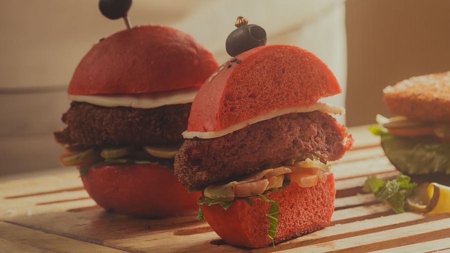 A close-up of a burger cut in half by a chef on a chopping board at Oasis, The Ananta Udaipur, showcasing the layers and ingredients.