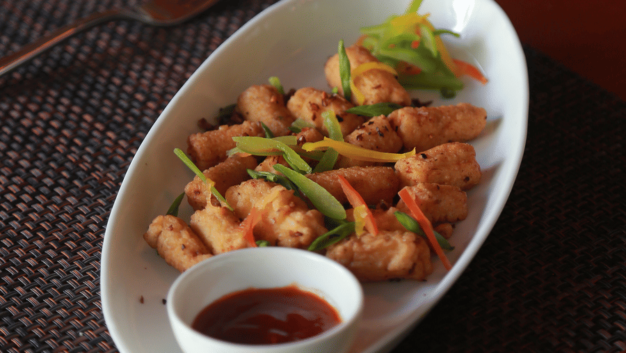 An overhead view of various appetisers, including crispy fried snacks and dipping sauces, served on long white plates at The Bull Boutique Hotel.