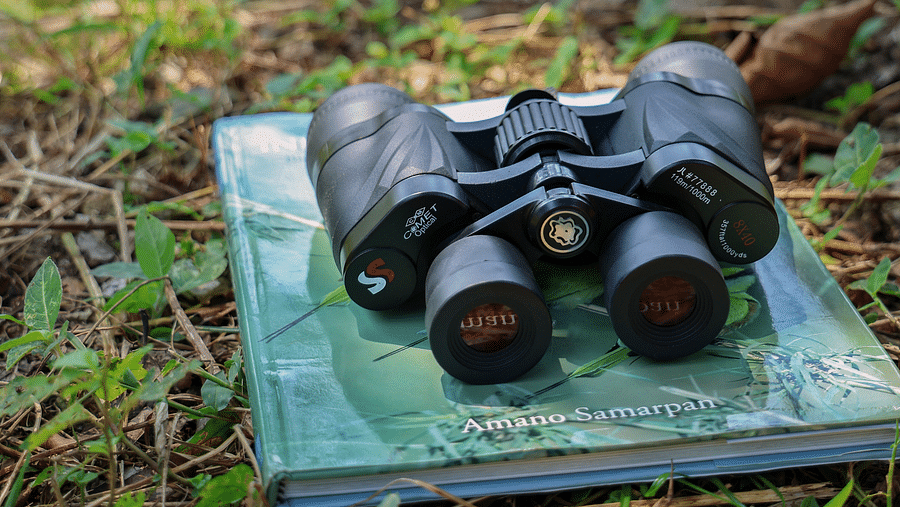 A pair of binoculars placed on a book on grass at The Sylvan Retreat, Dehradun.=