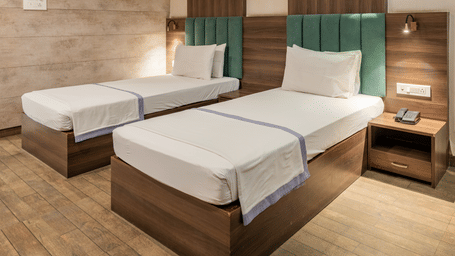 A closer view of the King Twin Room interior featuring two single beds side by side, wooden headboards, bedside tables, lamps, and framed artwork above the beds at Hotel Highway King, Behror.