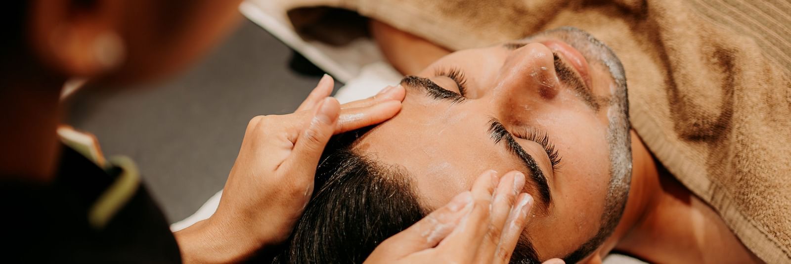 A spa staff member providing a head massage to a man relaxing on the bed at Crescent spa & resort, Indore
