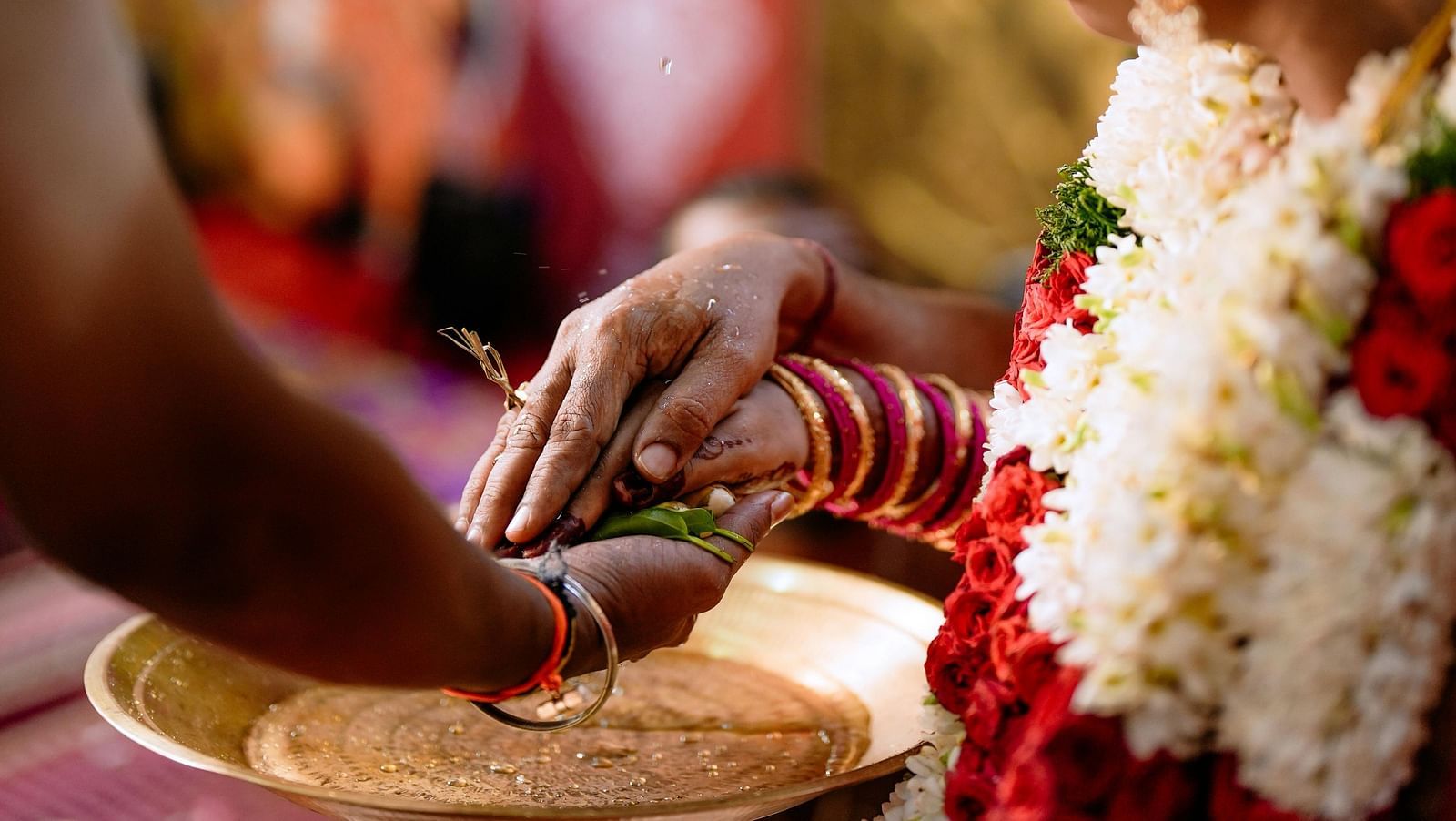 A wedding ceremony being performed with the priest where the bride and groom are holding their hands over a golden tray