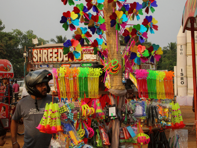 A street vendor's tall display filled with colourful toy pinwheels and trinkets against a backdrop.