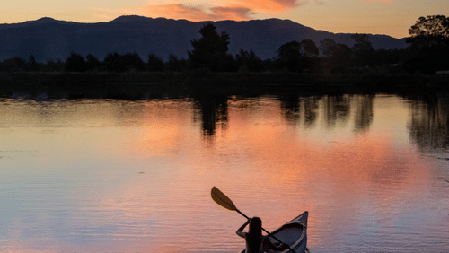 A person kayaking on a river with the sun setting behind it - Ramgarh Bungalows, Nainital.